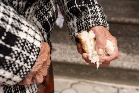Photo for Old woman's hands close-up, a piece of broken bread in the woman's hands, white bread and working human hands. Poverty and starving pensioners. - Royalty Free Image