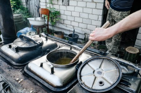 Foto de Un hombre prepara el almuerzo en una cocina militar, una gran espátula de madera para agitar la comida. - Imagen libre de derechos