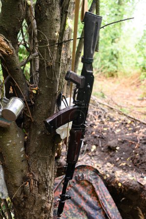 Foto de Un rifle automático cerca de una tienda en el bosque, una tienda militar en el bosque durante la guerra en Ucrania, las condiciones de vida de un soldado en guerra. - Imagen libre de derechos