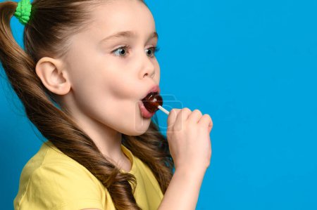 On a blue background, a girl licks a round lollipop close-up, caries and bad food for teeth.