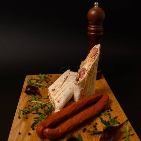 A sheet of pita bread with cabbage, carrots and hunting sausages on a wooden board, various salad leaves and pepper mill.
