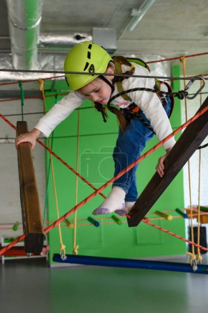 Photo for The girl carefully and carefully passes the cableway in the playroom, active recreation for children. - Royalty Free Image