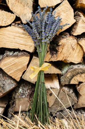 Téléchargez les photos : Un petit bouquet de lavande avec un ruban jaune sur fond de bois de chauffage. - en image libre de droit