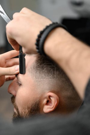 Téléchargez les photos : Le coiffeur fait le contour avec un rasoir dangereux lors de la coupe de cheveux undercut - en image libre de droit