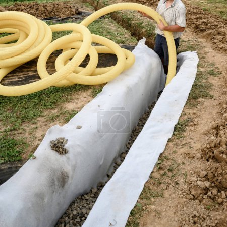 Photo for Groundwater drainage works in the field. A worker carries a yellow perforated drainage pipe. - Royalty Free Image