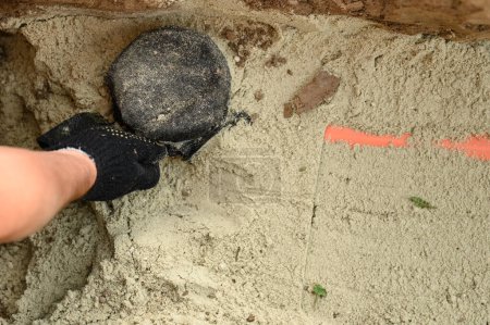 Téléchargez les photos : Un plombier installe un tuyau d'égout orange renforcé pendant l'entretien du site. Mains d'un plombier gros plan près d'un tuyau d'égout recouvert de sable. - en image libre de droit