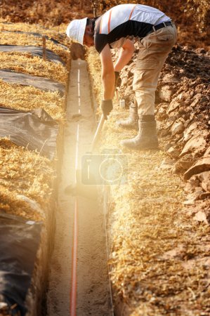 Téléchargez les photos : Un plombier installe un tuyau d'égout orange renforcé lors de l'entretien du site. - en image libre de droit