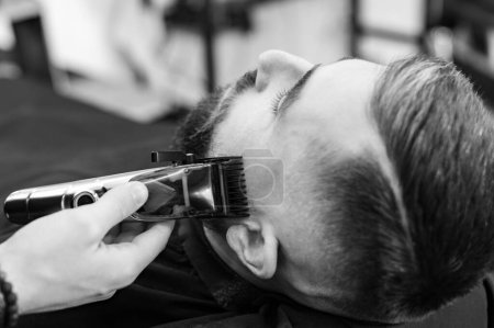 Foto de Cortar una barba de caballero en una barbería con un cortaplumas. Acortar la longitud de la barba de los lados por el maestro para el cliente. - Imagen libre de derechos