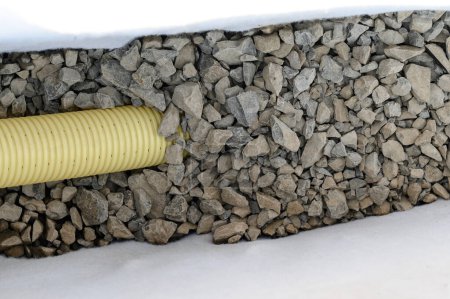 Tuyau ondulé jaune avec perforation dans une tranchée avec pierre concassée et géotextile. Travaux de drainage pour l'enlèvement des eaux souterraines sur le terrain.