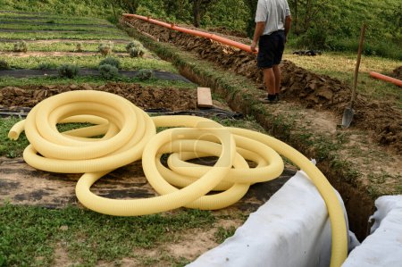 Foto de Trabajos de drenaje de aguas subterráneas en el campo. Un trabajador lleva una tubería de drenaje perforada amarilla. - Imagen libre de derechos