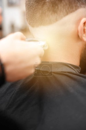 Foto de Peluquero afeita la sien con un recortador inalámbrico durante un corte de pelo corto en los lados de la cabeza. - Imagen libre de derechos