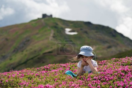 Ein kleines Mädchen sitzt auf einer Wiese voller Rhododendron, ein schönes Mädchen inmitten schöner Blumen in den Bergen.