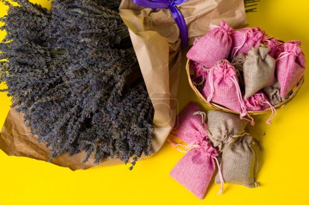 Dried lavender flowers and sachets on yellow background, lavender aromatherapy.