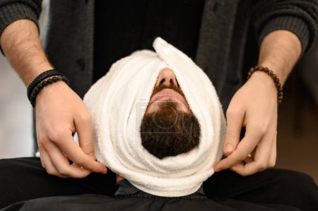 Le coiffeur couvre le visage des clients avec une serviette chaude et humide pour enlever la barbe.