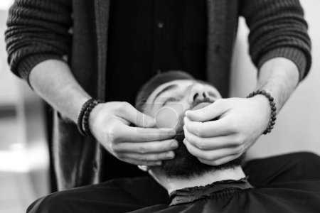 Ein Friseur massiert und reibt einem männlichen Kunden den Bart, nachdem er feuchtigkeitsspendendes Öl aufgetragen hat
