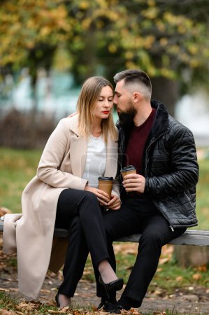 Una pareja, un hombre y una mujer, están sentados en el parque en un banco con café en sus manos, una reunión en el parque.