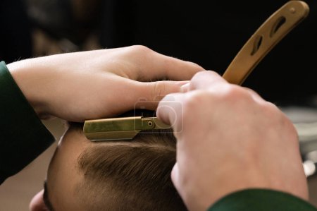 Foto de El peluquero hace el contorno con una máquina de afeitar peligrosa durante el corte de pelo undercut - Imagen libre de derechos