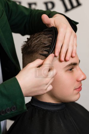 Haarstyling mit Kamm, Kämmen der Haare durch einen Stylisten. Haarschnitt eines Besuchers im Friseursalon.