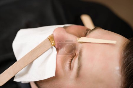 Nose hair wax removal. Hair removal procedure in a barbershop.