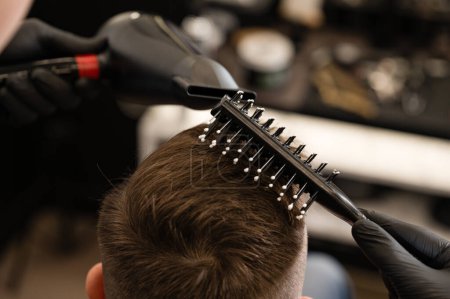 Haarstyling mit Kamm und Föhn mit Heißluft. Haarschnitt eines Besuchers im Friseursalon.
