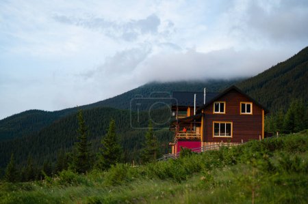 a girl in an orange jacket stands on the terrace of a wooden house against the background of mountains, a house for tourists in the Carpathians of Ukraine.