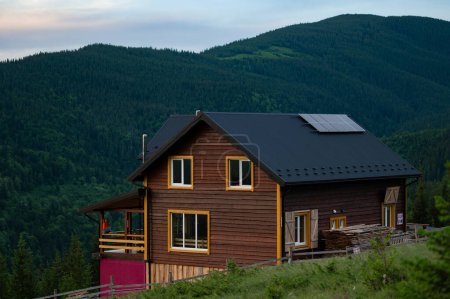 A large wooden house for tourists in the mountains, a young girl stands on the terrace against the background of the Carpathian Mountains, a house for recreation in the mountains.