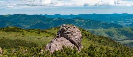 Dad and son are sitting on a big stone in the mountains, Vukhati Kamin mountain in the Carpathians of Ukraine, active recreation in the mountains in summer.