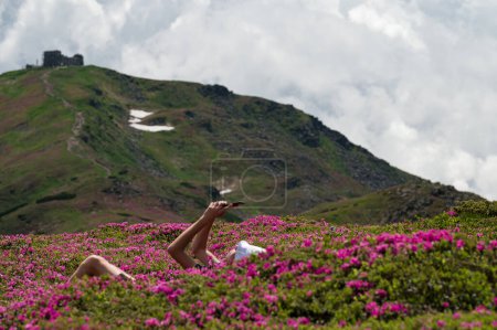 A guy with a white panama on his head sits between rhododendrons with a view of Pip Ivan, summer vacation in the Carpathians.
