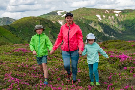 A mother with her son and daughter are walking among rhododendron bushes against the background of the majesty of the Carpathian Mountains, active summer vacation with children.