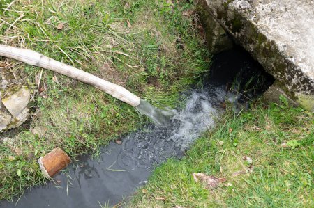 Water flows into the ditch from the hose, water under pressure flows from the hose.