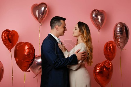 Photo for A woman in a dress and a man in a suit on the background of hearts balloons. Love on Valentine's Day, romance and love, dating on February 14. Beautiful young couple - Royalty Free Image