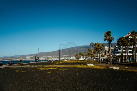 Foto de Playa de las Americas, Tenerife Spain. 12/17/2022 Beach at sunset under palm trees, sunbeds and sun, summer day and vacation, mountains. A city in the mountains - Imagen libre de derechos