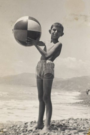 Téléchargez les photos : Enfant garçon jouant avec une balle sur la plage en 1953, Italie. photographie d'archives, noir et blanc. - en image libre de droit