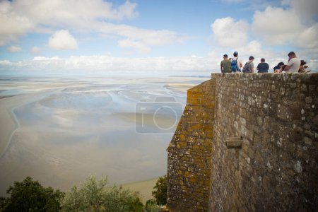 Photo for MONT SAINT MICHEL, AUGUST 2023 - Tourists admiring the view of the bay with low tide, from Mont Saint Michel Abbey walls on a summer day. - Royalty Free Image