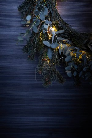 Foto de Sección de guirnalda de Navidad de pino y eucalipto, con luces de cuerda iluminadas. Fondo con espacio de copia. Disparo vertical. - Imagen libre de derechos