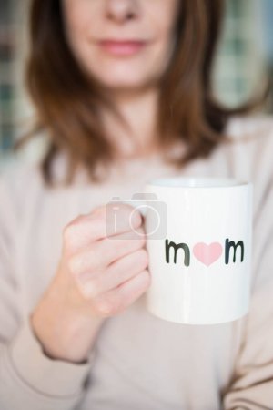 Foto de Mujer caucásica, sonriendo feliz por ser madre, sosteniendo una taza del día de la madre con "mamá" escrita en ella. Rosa, fondo aireado. - Imagen libre de derechos