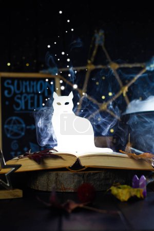 Leuchtende, leuchtende Katzenfigur, die in einem magischen Stillleben mit Tafel und Hexenkessel einem Buch entsteigt. Hexerei, gönnerhafter Hintergrund. Vertikal.