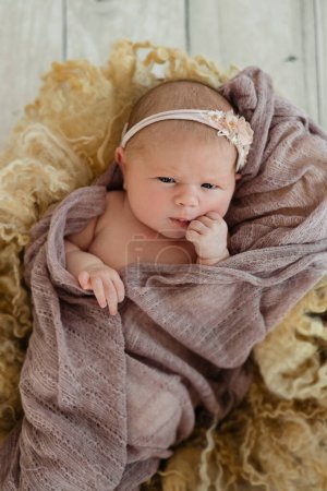 Un nouveau-né avec un sourire sur le visage est assis sur une table en bois, enveloppé dans une couverture confortable en matériau naturel pour le confort et la chaleur