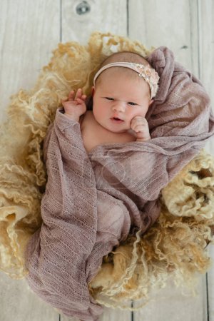 Un nouveau-né avec un sourire sur le visage est assis sur une table en bois, enveloppé dans une couverture confortable en matériau naturel pour le confort et la chaleur