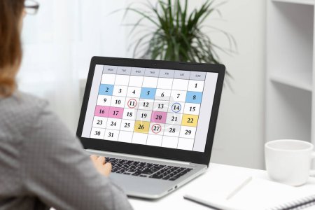 Téléchargez les photos : Femme planifiant des réunions d'affaires mensuelles, le calendrier et les objectifs en utilisant le calendrier sur ordinateur portable. - en image libre de droit