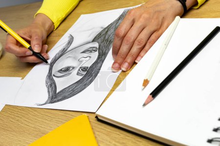 Téléchargez les photos : L'artiste dessine un portrait au crayon d'une jeune belle femme. Le concepteur crée une image d'une fille sur papier blanc. - en image libre de droit