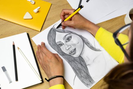 Téléchargez les photos : L'artiste dessine un portrait au crayon d'une jeune belle femme. Le concepteur crée une image d'une fille sur papier blanc. - en image libre de droit