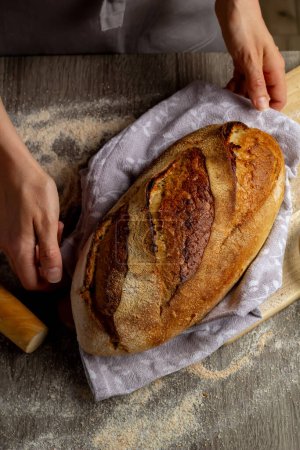 Téléchargez les photos : Gros plan de pain fraîchement cuit dans les mains sur un fond de planche en bois. - en image libre de droit