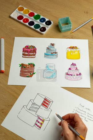 Téléchargez les photos : Le pâtissier développe un design de gâteau en dessinant sur papier. Création de produits de confiserie. - en image libre de droit