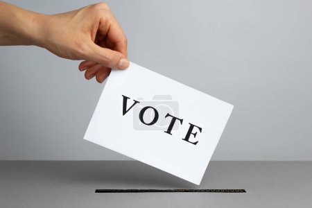 Téléchargez les photos : Une main jette un bulletin de vote dans une urne le jour du scrutin. Concept de vote. - en image libre de droit