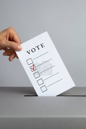 Téléchargez les photos : Une main jette un bulletin de vote dans une urne le jour du scrutin. Concept de vote. - en image libre de droit