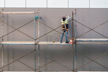 Construction worker on the scaffold prepares house facade wall for painting