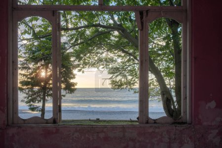 View of a sunset seascape from broken window in an abandoned house with pink walls