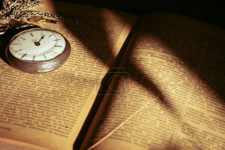 Antique pocket watch and ancient open book. Retro style objects. Vintage silver clock with chain on book. Nostalgia concept. The past background. Watch mechanism close up. Literature background.