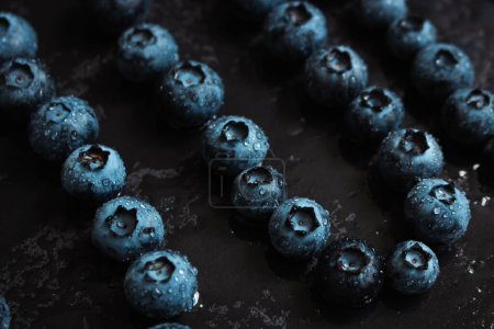 Wet blueberries on black cutting board. Forest berries with water drops on the table. Blueberries isolated. Summer harvest. Vitamin and antioxidant concept. Juicy dessert. Fresh ripe berries. Organic food. 